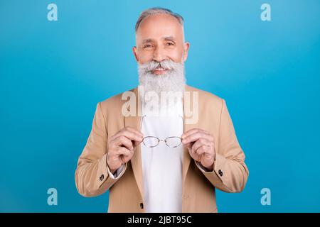Ritratto di bell'elegante e allegro uomo grigio-pelo che tiene in mano specs isolato su sfondo di colore blu brillante Foto Stock