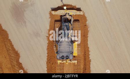 Bulldozer giallo che sparge il terreno sulla sabbia. Vista dal basso del drone aereo. Foto di alta qualità Foto Stock