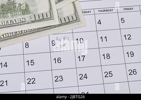 Giorno d'imposta segnato in calendario con banconote in dollari. Vista dall'alto, disposizione piatta. Foto Stock