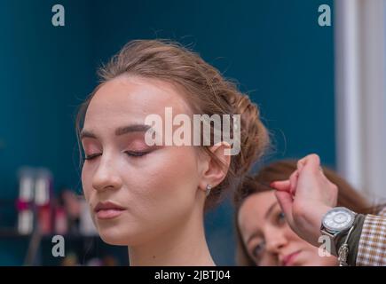 Il volto della ragazza di un cliente, da dietro il padrone esamina i suoi capelli in sfocatura. Il parrucchiere crea un'acconciatura per una giovane donna. Barbiere, concetto di business. Salone di bellezza, cura dei capelli. Foto Stock