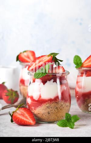 Cheesecake alla fragola. Cheesecake o trifle con fragola in vetro su sfondo vecchio tavolo grigio cemento. Cheesecake senza cottura. Dess Foto Stock