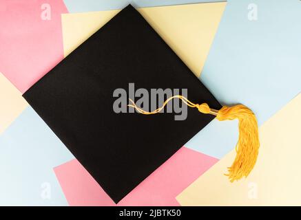 Cappello o cappello nero con nappina gialla su sfondo pastello colorato per l'istruzione Foto Stock