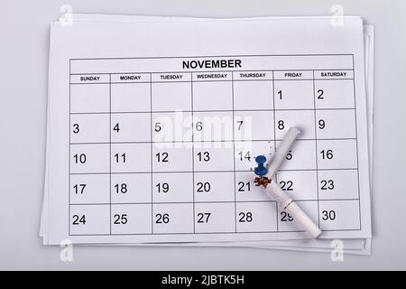 Sigaretta rotta con spilla sul calendario del mese. Calendario di novembre su sfondo bianco. Foto Stock