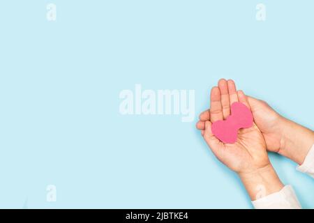 Le mani della donna tengono carta rosa a forma di ghiandola tiroidea su uno sfondo azzurro con spazio di copia Foto Stock