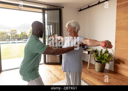 Fisioterapista maschile afroamericano che aiuta la donna anziana caucasica a fare esercizio con i manubri Foto Stock