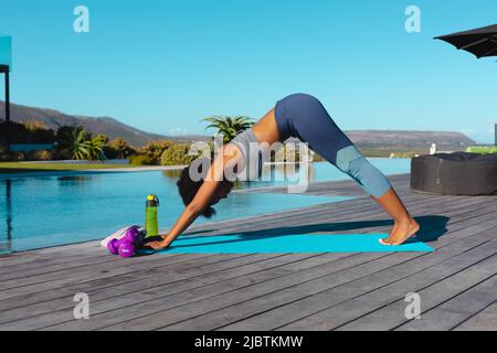 Giovane donna afroamericana che pratica yoga all'aperto vicino alla piscina Foto Stock