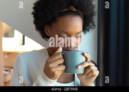 Primo piano della giovane donna afroamericana che beve caffè a casa Foto Stock