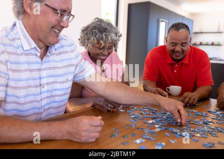 Sorridente multirazziale anziani amici che arrangiano pezzi su tavola di legno in casa di riposo Foto Stock