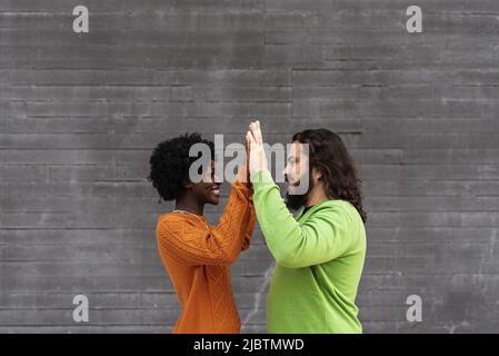 Felice coppia interrazziale che si guarda l'un l'altro e unire le mani mentre si alza all'aperto. Foto Stock