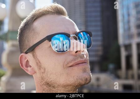 Riflessione dei grattacieli in occhiali da sole del giovane uomo. Turista ammirando edifici storici in città. Temi del turismo e della protezione degli occhi. Foto Stock