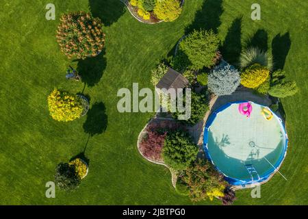 Giardino splendidamente paesaggistico al cortile con piscina e prato perfettamente mantenuto. Giardiniere professionista al lavoro che prende cura delle piante. H Foto Stock