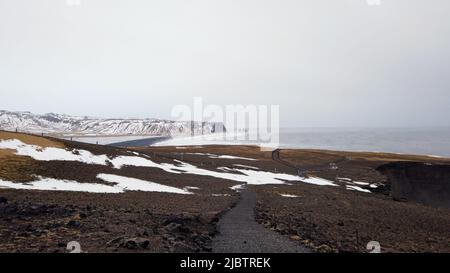 Vista dal faro di Dyrholaey in Islanda con vista sulla spiaggia di sabbia nera sottostante durante l'inverno con neve e bel tempo di sole. Foto Stock