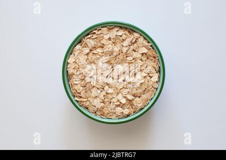 Vista dall'alto di fiocchi di avena sani e nutrienti in un recipiente verde. Cibo cerealicolo popolare isolato su sfondo bianco, fuoco selettivo. Foto Stock