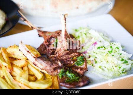 deliziosi bastoncini di agnello alla griglia con patatine fritte, salsa di pesto e un mix di lattughe Foto Stock