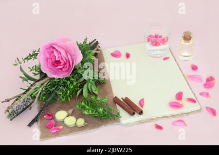 Streghe amore pozione ricetta incantesimo con fiore di rosa, bundle erbe, quarzo cristallo, acqua di sorgente, canapa ricetta notebook, bottiglia d'olio, zenzero e cannella. Foto Stock