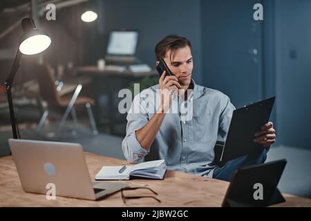 giovane uomo d'affari con una clipboard che parla su uno smartphone. Foto Stock