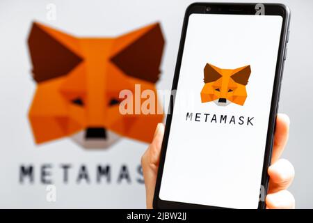 Ucraina, Odessa - Ottobre, 9 2021: Tenere la mano mobile con l'app MetaMask in esecuzione sullo schermo dello smartphone con il logo MetaMask sullo sfondo. MetaMask è un software di crittografia portafoglio Foto Stock