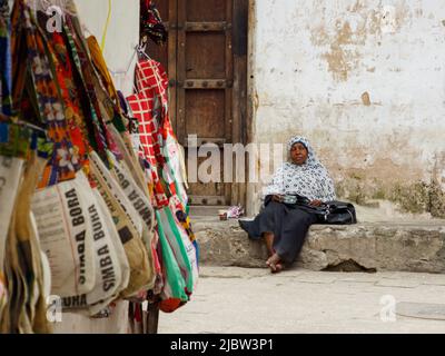 Città di pietra, Zanzibar, Tanzania - Gennaio 2021: Anziana donna africana pensiva seduta tra le mura di pietra della città africana Foto Stock