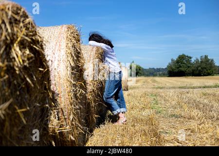 donna appoggiata su balle di paglia nel campo guardando il cielo blu estivo Foto Stock