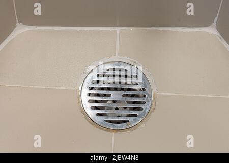 il pavimento in piastrelle con una griglia sul foro di scarico in bagno con doccia, primo piano Foto Stock