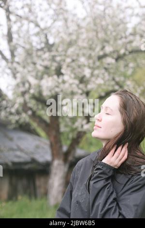 ritratto emozionale di una giovane donna in piedi sola sotto la pioggia all'aperto in primavera. Foto Stock