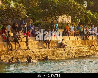 Città di pietra, Zanzibar, Tanzania - Jan 2021: Folla della gente sui giardini di Forodhani e bambini che saltano in acqua da un muro durante il tramonto. C Foto Stock