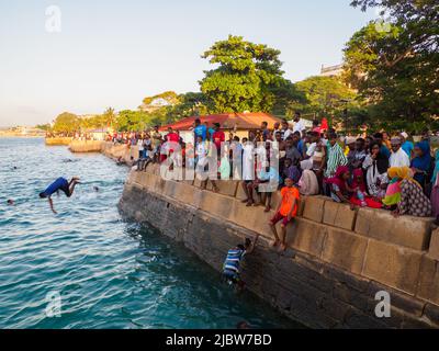 Città di pietra, Zanzibar, Tanzania - Jan 2021: Folla della gente sui giardini di Forodhani e bambini che saltano in acqua da un muro durante il tramonto. C Foto Stock