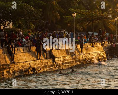 Città di pietra, Zanzibar, Tanzania - Jan 2021: Folla della gente sui giardini di Forodhani e bambini che saltano in acqua da un muro durante il tramonto. C Foto Stock