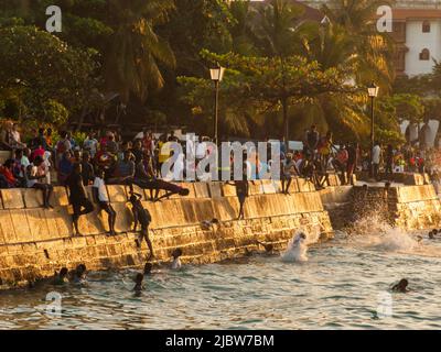 Città di pietra, Zanzibar, Tanzania - Jan 2021: Folla della gente sui giardini di Forodhani e bambini che saltano in acqua da un muro durante il tramonto. C Foto Stock