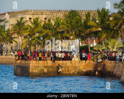 Città di pietra, Zanzibar, Tanzania - Jan 2021: Folla della gente sui giardini di Forodhani e bambini che saltano in acqua da un muro durante il tramonto. C Foto Stock