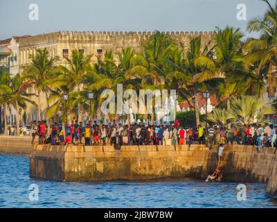 Città di pietra, Zanzibar, Tanzania - Jan 2021: Folla della gente sui giardini di Forodhani e bambini che saltano in acqua da un muro durante il tramonto. C Foto Stock