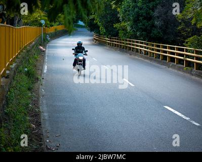 Medellin, Antioquia, Colombia - Gennaio 19 2022: Moto su una strada asfaltata nel mezzo di una foresta Foto Stock