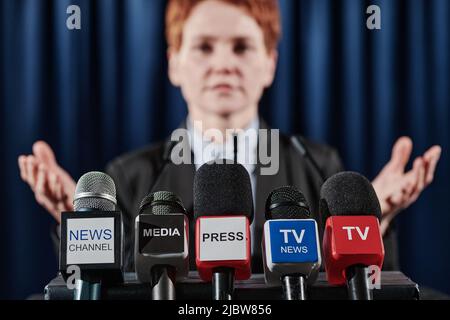 Primo piano di microfoni di vari mezzi televisivi con altoparlante in piedi dietro di loro a tribune Foto Stock