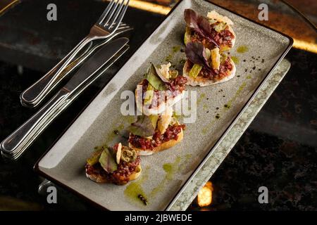 Quattro bruschette con tartare di manzo su un piatto, crostini con tartare di manzo, bruschetta di manzo, sandwich con manzo crudo gourmet Foto Stock