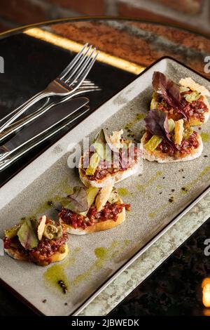 Quattro bruschette con tartare di manzo su un piatto, crostini con tartare di manzo, bruschetta di manzo, sandwich con manzo crudo gourmet Foto Stock