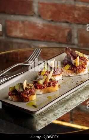 Quattro bruschette con tartare di manzo su un piatto, crostini con tartare di manzo, bruschetta di manzo, sandwich con manzo crudo gourmet Foto Stock