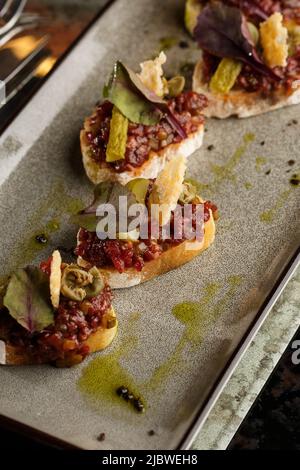 Quattro bruschette con tartare di manzo su un piatto, crostini con tartare di manzo, bruschetta di manzo, sandwich con manzo crudo gourmet Foto Stock