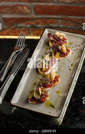 Quattro bruschette con tartare di manzo su un piatto, crostini con tartare di manzo, bruschetta di manzo, sandwich con manzo crudo gourmet Foto Stock
