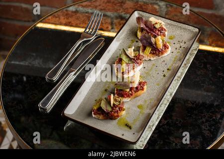 Quattro bruschette con tartare di manzo su un piatto, crostini con tartare di manzo, bruschetta di manzo, sandwich con manzo crudo gourmet Foto Stock