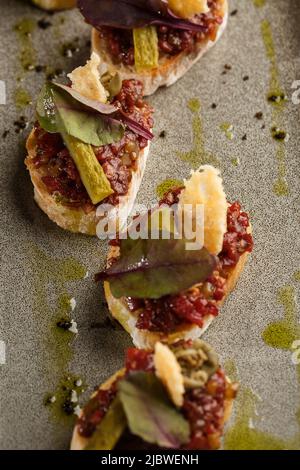 Quattro bruschette con tartare di manzo su un piatto, crostini con tartare di manzo, bruschetta di manzo, sandwich con manzo crudo gourmet Foto Stock