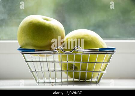 Due mele verdi mature si trovano in un cestino dal supermercato sulla finestra della casa in cucina Foto Stock