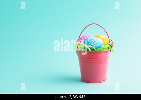 Pasqua uova colorate in secchio decorativo rosso isolato su sfondo blu pastello con spazio copia. Vista frontale, concetto di saluto. Foto Stock