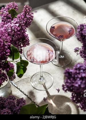 Due bicchieri da vino rosa con fiori lilla e ombre su sfondo grigio. Drink estivo per feste, vinerie, menu o degustazione Foto Stock