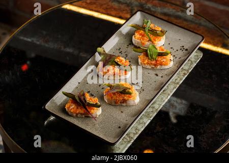 bruschetta al forno con salmone, formaggio, pomodori secchi e avocado in piatto grigio su sfondo luminoso. Foto Stock