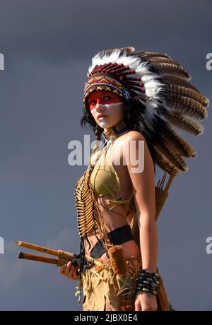 Una donna indiana americana nativa è vista in piedi di fronte a tempeste grigie. Indossa un headdress piume ed ha vestito indiano tradizionale sopra. Foto Stock