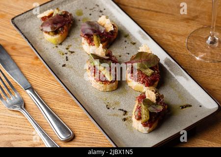 Quattro bruschette con tartare di manzo su un piatto, crostini con tartare di manzo, bruschetta di manzo, sandwich con manzo crudo gourmet Foto Stock