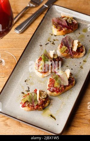 Quattro bruschette con tartare di manzo su un piatto, crostini con tartare di manzo, bruschetta di manzo, sandwich con manzo crudo gourmet Foto Stock