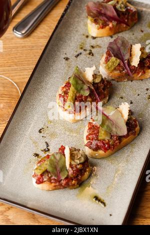 Quattro bruschette con tartare di manzo su un piatto, crostini con tartare di manzo, bruschetta di manzo, sandwich con manzo crudo gourmet Foto Stock