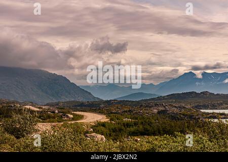 Skagway, Alaska, USA - 20 luglio 2011: Autostrada Klondike per il Canada. La strada sterrata si snoda attraverso il paesaggio selvaggio sotto il paesaggio nuvoloso marrone con il canadese Foto Stock