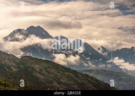 Skagway, Alaska, USA - 20 luglio 2011: Autostrada Klondike per il Canada. Dark Canadian Rocky Peaks, con zone innevate e circondato da paesaggi nuvolosi. Venatura verde Foto Stock